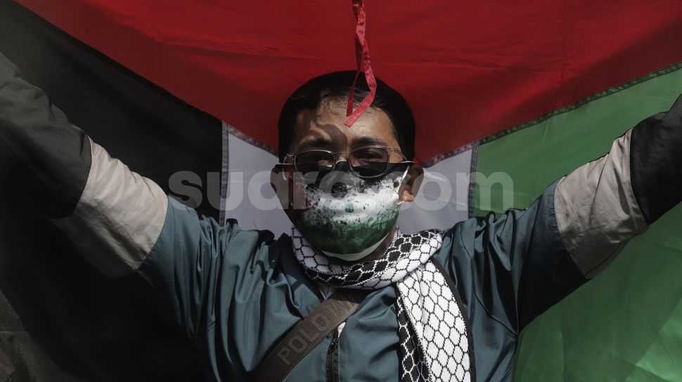 Seorang massa aksi membawa bendera Palestina saat mengikuti aksi solidaritas dukung Palestina terkait kekerasan yang terjadi beberapa waktu lalu oleh Israel di depan Kedubes AS, Jakarta, Selasa (18/5/2021). [Suara.com/Angga Budhiyanto]