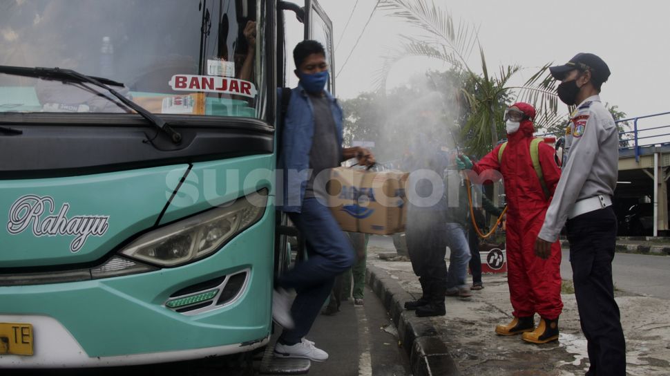 Petugas menyemprotkan cairan disinfektan kepada pemudik yang baru tiba di Terminal Kampung Rambutan, Jakarta, Jumat (21/5/2021). [Suara.com/Dian Latifah]