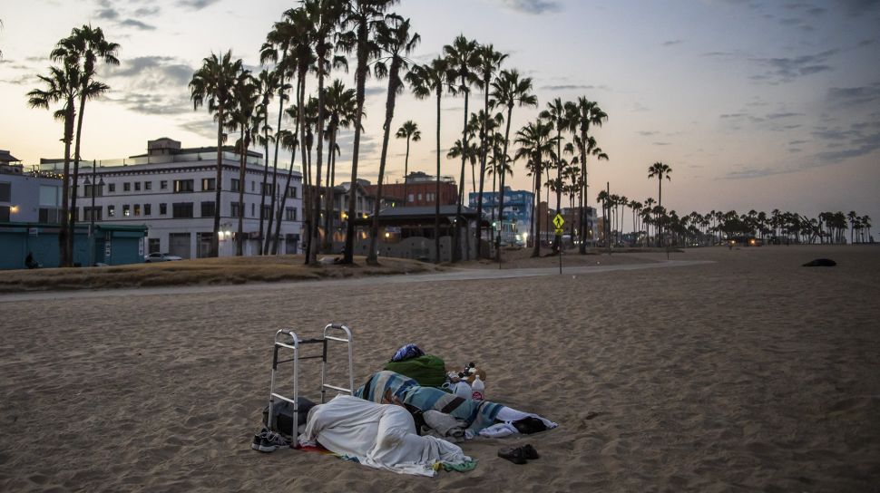 Dua orang tunawisma tidur di pantai pada pagi hari di Pantai Venesia, California, Amerika Serikat, pada (12/8/2021). [Apu GOMES / AFP]