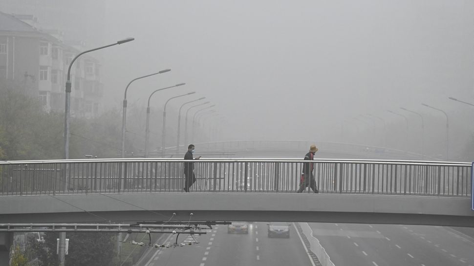 Orang-orang memakai masker berjalan di jalan layang pada hari yang berkabut dan tercemar di Beijing, China, Sabtu (6/11/2021). [JADE GAO / AFP]