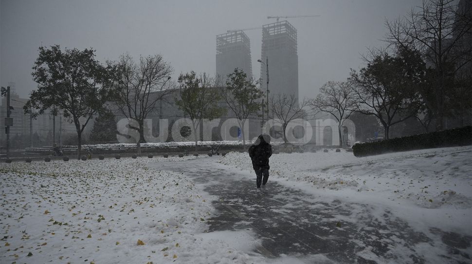 Seorang warga menggunakan kantong plastik sebagai penutup saat salju turun di Beijing, China, Minggu (7/11/2021). [NOEL CELIS / AFP]