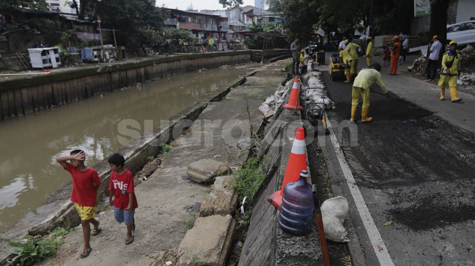 Dua orang anak berjalan di samping perbaikan jalan ambles di Jalan Inspeksi Kali Ciliwung, Kenari, Kecamatan Senen, Jakarta, Rabu (19/1/2022). [Suara.com/Angga Budhiyanto]