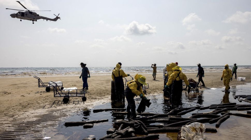 Sebuah helikopter terbang di atas para pekerja yang sedang membersihkan tumpahan minyak mentah di Pantai Mae Ram Phueng, menyusul tumpahan yang disebabkan oleh kebocoran pipa bawah laut milik Star Petroleum Refining Public Company Limited (SPRC) di Rayong, Thailand, Sabtu (29/1/2022). [JACK TAYLOR / AFP]