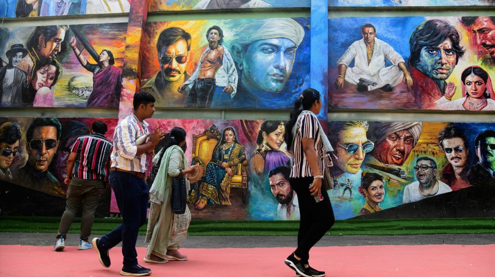 Orang-orang berjalan melewati mural bergambar aktor Bollywood saat mengunjungi Taman Bollywood di Filmcity Mumbai, India, Jumat (13/5/2022). [SUJIT JAISWAL / AFP]