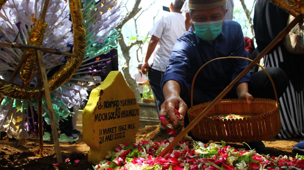 Seorang pelayat menaburkan bunga di atas makam almarhum Achmad Yurianto di pemakaman umum Dadaprejo, Batu, Jawa Timur, Minggu (22/5/2022).  ANTARA FOTO/Ari Bowo Sucipto
