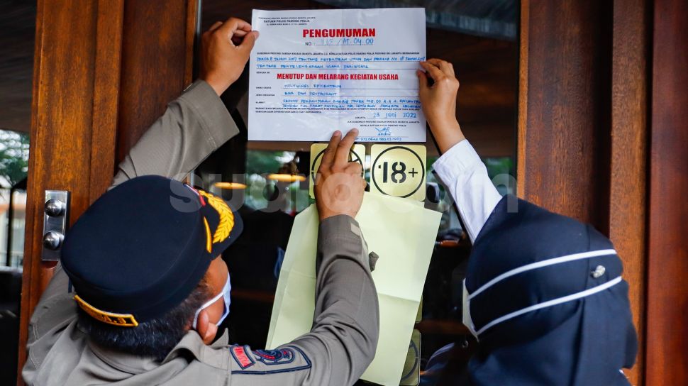 Petugas Satuan Polisi Pamong Praja (Satpol PP) saat menempelkan sticker berisi informasi penutupan dan penyegelan outlet Holywings Epicentrum di Kuningan, Jakarta Selatan, Selasa (28/6/2022). [Suara.com/Alfian Winanto]