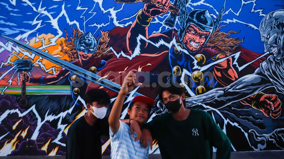 Warga berswafoto di dekat mural kolaborasi bergambar Thor di Terowongan Kendal, Jakarta Pusat, Selasa (5/7/2022). [Suara.com/Alfian Winanto]