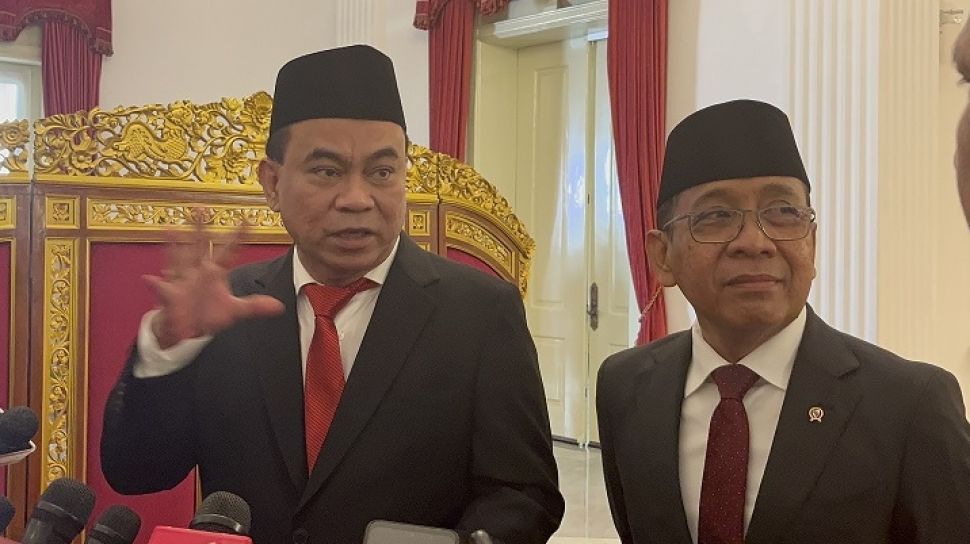  Two men in suits and traditional headdresses are having a discussion with one man gesturing while the other is looking straight at the camera. The image shows the SAFEnet petition for Budi Arie Setiadi's resignation over cybersecurity concerns in Indonesia.