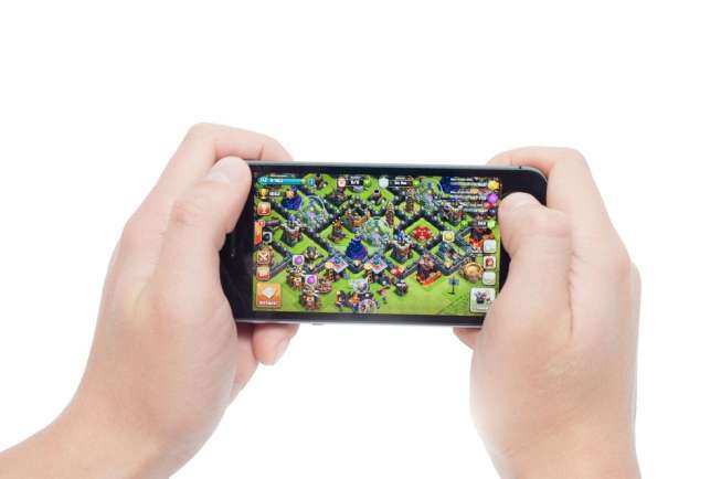 Ilustrasi pengguna ponsel pintar sedang bermain game Clash of Clans (Shutterstock).