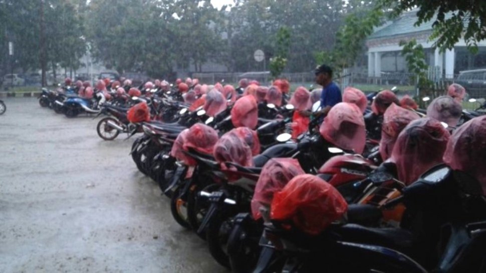 Tukang parkir dan helm-helm di sepeda motor yang sudah diberinya bungkusan plastik di tengah hujan. [Akun Facebook Bintang/capture]