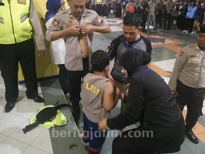 Iptu Sugik Hernawan melepas bajunya untuk diberikan ke Aremania cilik yang tak pakai baju dan kuyub karena hujan serta terlepas dari orangtuanya. [Beritajatim]