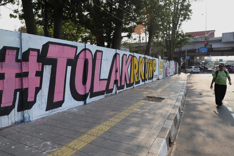 Warga melintas di depan mural bertuliskan "#Tolak RKUHP" di kawasan Rawamangun, Jakarta Timur, Sabtu (28/9). [Suara.com/Angga Budhiyanto]