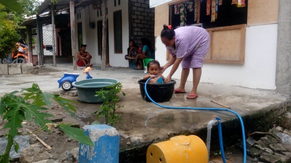 Seorang warga Jrebeng saat memandikan anaknya dengan air PDAM milik BUMdes Jrebeng dari bendungan Bengawan yang keruh dan bau saat musim kemarau, Sabtu (2/11/2019). [Suara.com/Tofan Kumara]