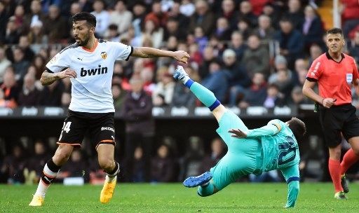 Pemain Valencia Ezequil Garray menjatuhkan pemain Barcelona Lionel Messi dalam laga di Estadio Mestalla, Sabtu (25/1/2020). [AFP]