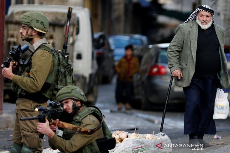 Seorang pria Palestina melihat tentara Israel membidikkan senjata ke arah pengunjuk rasa yang menentang rancangan perdamaian Timur Tengah Presiden Amerika Serikat Donald Trump, di Hebron, wilayah penjajahan Israel, Tepi Barat, Kamis (6/2/2020). ANTARA FOTO/REUTERS/Mussa Qawasma/ama/djo