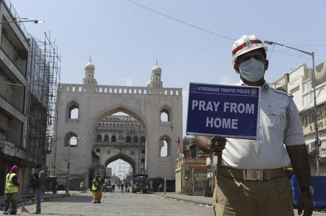 Seorang polisi lalu lintas di salah satu sudut Kota New Delhi, India menunjukkan imbauan agar berdoa dari rumah selama wabah virus corona. (Foto: AFP)