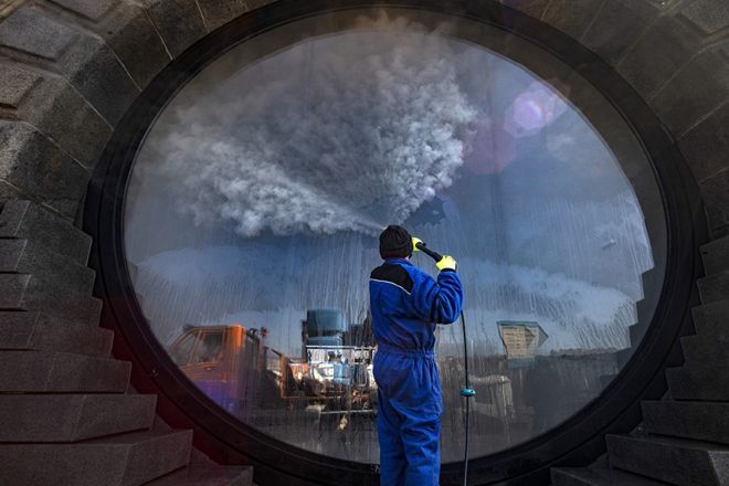 Seorang pekerja menyemprotkan cairan disinfektan ke jendela di sepanjang tepi sungai Vltava sebagai bagian dari upaya untuk membendung penyebaran Covid-19 di Praha, Republik Ceko. (MICHAL CIZEK / AFP)
