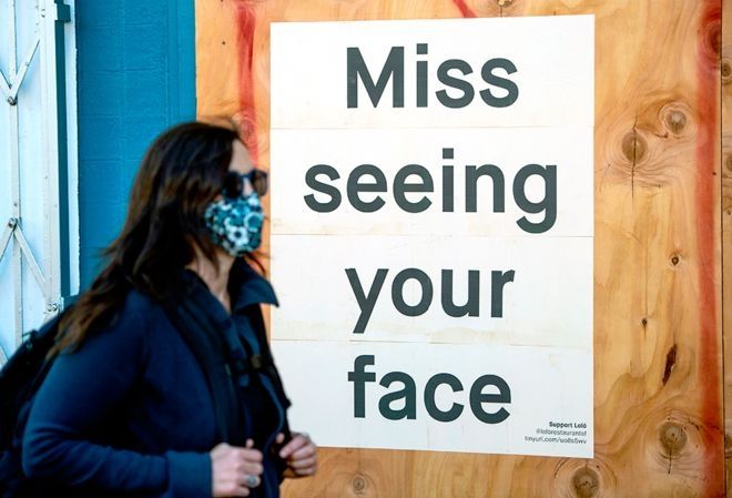Seorang perempuan mengenakan masker berjalan melewati papan iklan yang dipasang di sebuah restoran di San Francisco, California. (JOSH EDELSON / AFP)