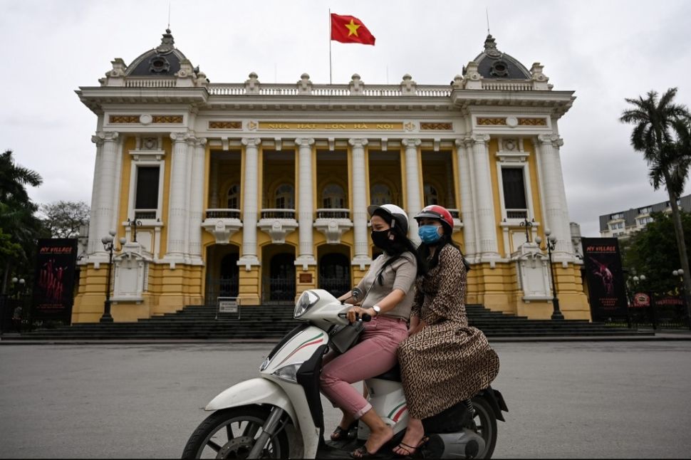 Pengendara motor mengenakan masker saat berkendara melewati Opera House di Hanoi, Vietnam, Kamis (23/4/2020). [AFP/Manan Vatsyayana]