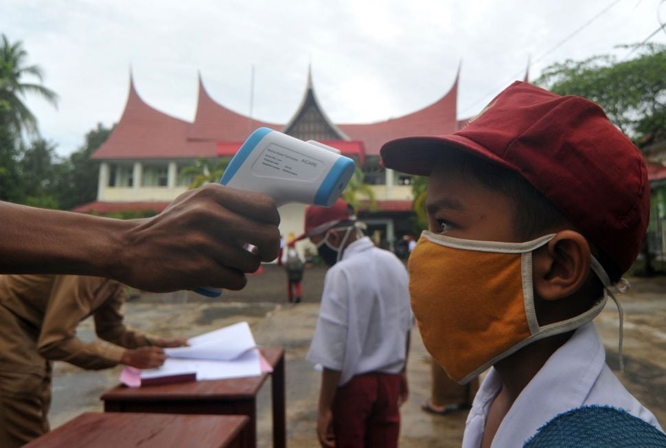 Guru memeriksa suhu tubuh murid saat hari pertana masuk sekolah di SDN 11 Marunggi, Pariaman, Sumatera Barat, Senin (13/7/2020). [Foto/Antara]