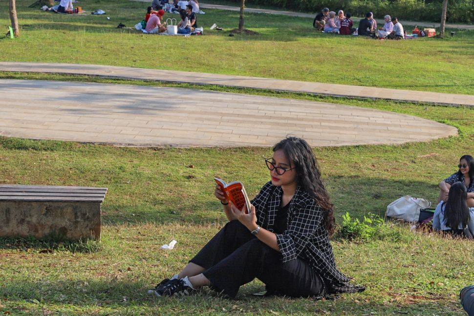 Seorang warga menghabiskan waktinya dengan membaca buku di area Hutan Kota Gelora Bung Karno, Senayan, Jakarta Sekatan, Minggu (23/8). [Suara.com/Alfian Winanto]