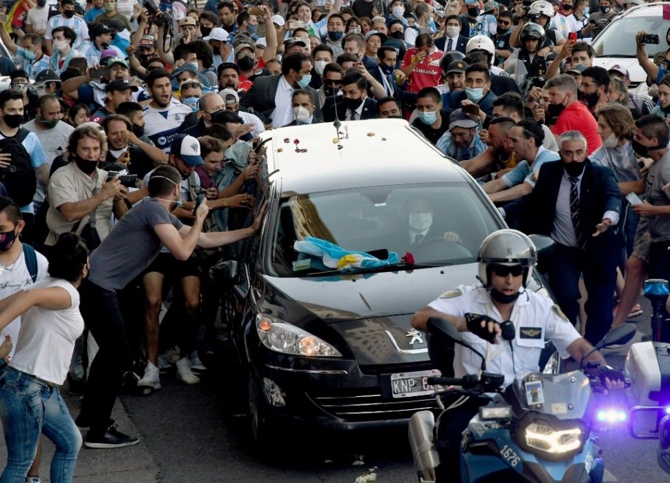 Foto yang dirilis Telam menunjukkan para penggemar berkerumun di samping mobil jenazah yang membawa mendiang legenda sepak bola Argentina Diego Armando Maradona dalam perjalanan dari istana kepresidenan Casa Rosada ke pemakaman  Jardin Bella Vista, di Buenos Aires pada Kamis (26/11/2020) waktu setempat. [Raul FERRARI / TELAM / AFP]