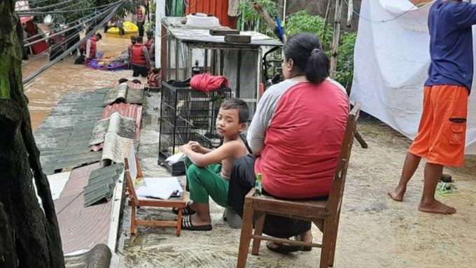 Ibu Ilah mengawasi anaknya yang belajar online di atap rumah, saat kebanjiran. Kawasan Kelurahan Cipinang Melayu, khususnya di RW04, Jakarta Timur, dilanda banjir setinggi 1 meter hingga 3 meter, Jumat (20/2/2021). [Suara.com/Bagaskara Isdiansyah]