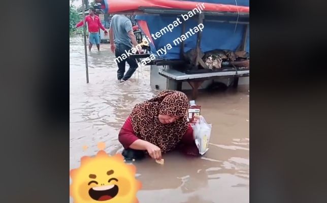 Emak-emak makan biskuit di tengah genangan banjir. [TikTok]