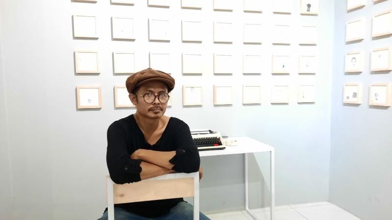 Syam Terrajana berfoto di depan lukisan dan karyanya yang dipamerkan di Pameran Tunggal bertema Pada Ruang yang Bercerita di Ruangdalam Art House, Gang Sawo no 55, Padukuhan Jeblog, Kalurahan Tirtonirmolo, Kapanewon Kasihan, Bantul, Jumat (5/3/2021). [Muhammad Ilham Baktora / SuaraJogja.id]