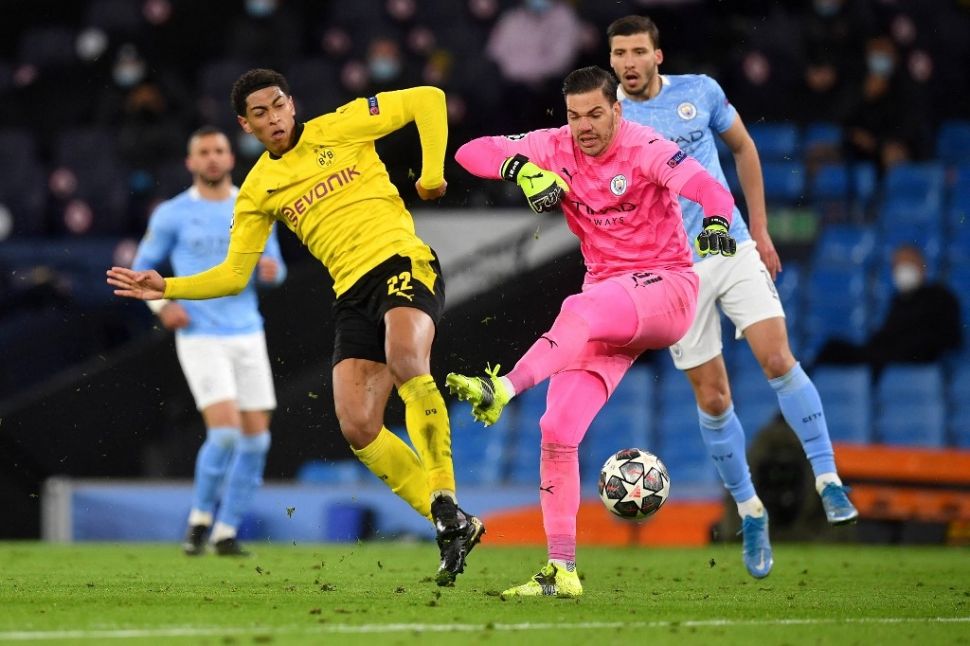 Gelandang Borussia Dortmund, Jude Bellingham (kir) mencetak gol yang pada akhirnya dianulir wasit karena dianggap lebih dulu melanggar kiper Manchester City Ederson Moraes dalam laga leg pertama perempat final Liga Champions 2020/2021 di Etihad Stadium, Rabu (7/4/2021) dini hari WIB. [Paul ELLIS / AFP].