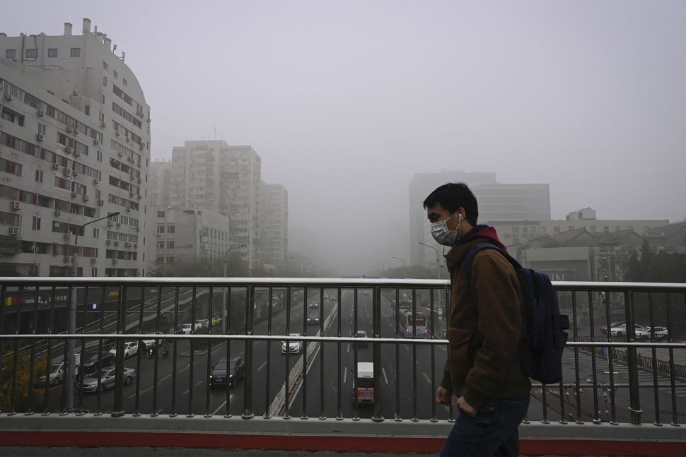 Warga memakai masker berjalan di jalan layang pada hari yang berkabut dan tercemar di Beijing, China, Sabtu (6/11/2021). [JADE GAO / AFP]