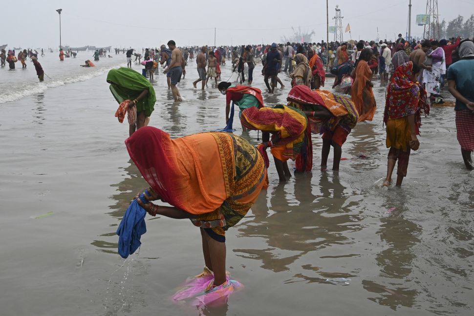 Peziarah Hindu mencuci pakaian mereka setelah berenang suci di pertemuan Gangga dan Teluk Benggala selama Gangasagar Mela pada kesempatan Makar Sankranti di Pulau Sagar, India, pada (14/1/2022). [DIBYANGSHU SARKAR / AFP]