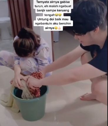 Momen sepasang kekasih membersihkan air yang menggenang akibat si perempuan yang coba membantu mencuci. (TikTok/amelcntkk27)