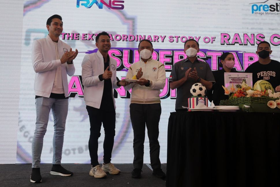 Raffi Ahmad (kedua kiri) memberikan potongan tumpeng pada Menteri Pemuda dan Olahraga Zainudin Amali (ketiga kiri) saat acara "Superstar Announcement RANS Cilegon FC" di kantor Prestige Motorcars, Pluit, Jakarta, Selasa (29/3/2022). [Suara.com/Angga Budhiyanto]