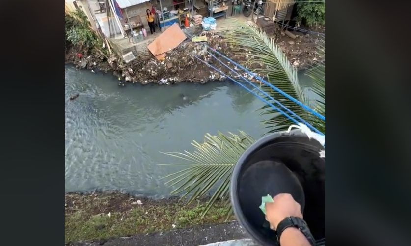 Perempuan pedagang gorengan memakai tali dan ember untuk layani pembeli di seberang sungai. [TikTok]