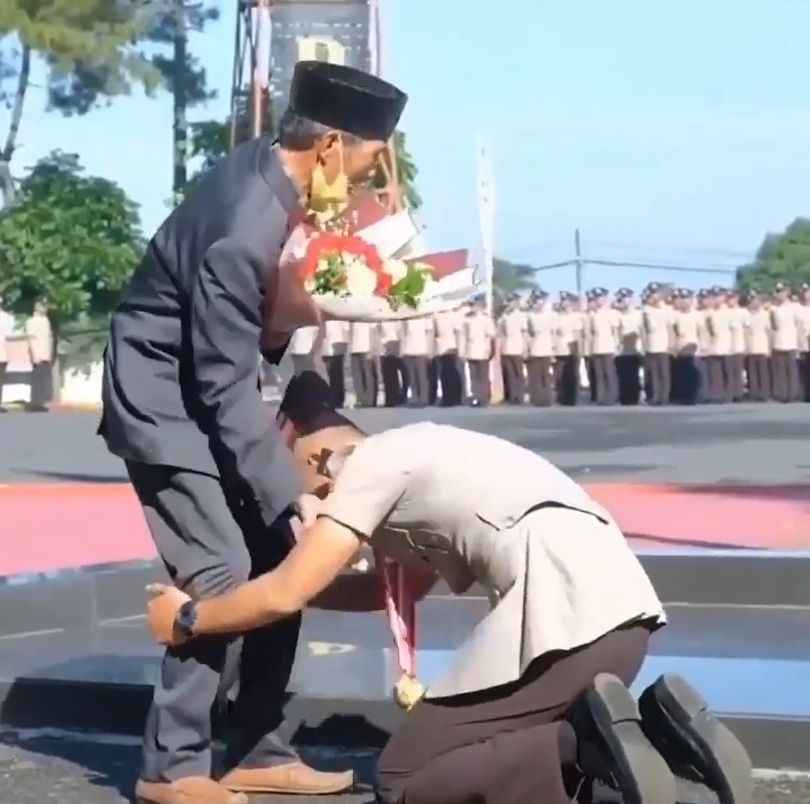 Seorang pemuda yang baru lulus pendidikan polisi sujud di kaki sang ayah. [Instagram]