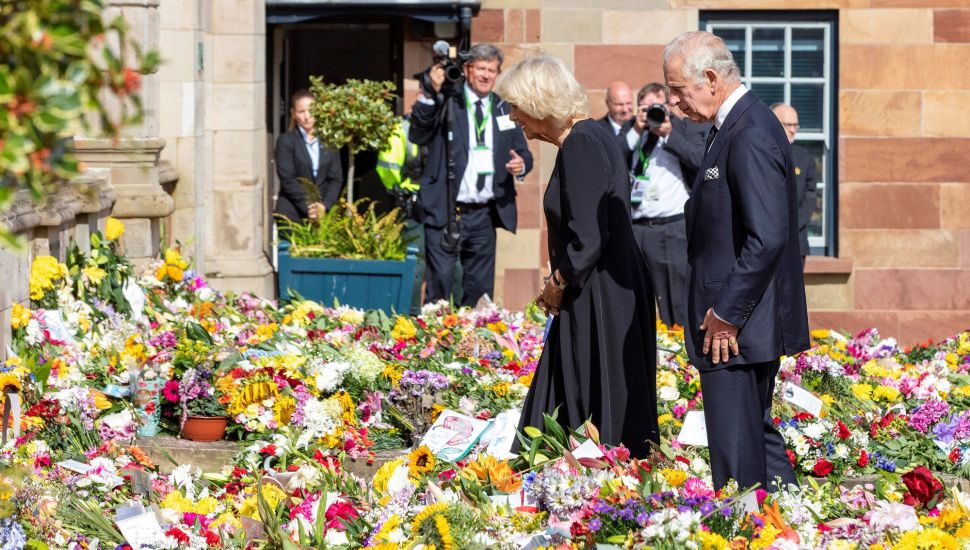 Raja Inggris Charles III dan Permaisuri Camilla melihat karangan bunga yang diberikan masyarakat di luar Kastil Hillsborough, Belfast, Irlandia Utara, Selasa (13/9/2022). [Niall Carson / POOL / AFP]