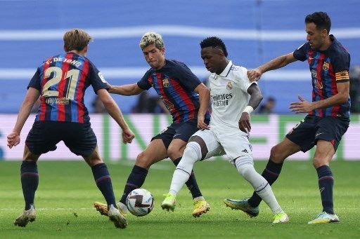 Tiga pemain Barcelona Frenkie de Jong (kiri), Ronald Araujo dan Sergio Busquets (kanan) mencoba menghentikan laju pemain Real Madrid Vinicius Junior (tengah) dalam pertandingan pekan ke-9 La Liga di Santiago Bernabeu, Minggu (16/10/2022). [AFP]