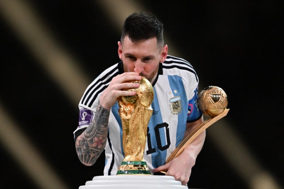 Penyerang Timnas Argentina, Lionel Messi sambil memegang trofi bola emas sebagai pemain terbaik Piala Dunia 2022, mencium trofi Piala Dunia di Stadion Lusail, Qatar, Senin (19/12/2022) dini hari WIB. [Kirill KUDRYAVTSEV / AFP]