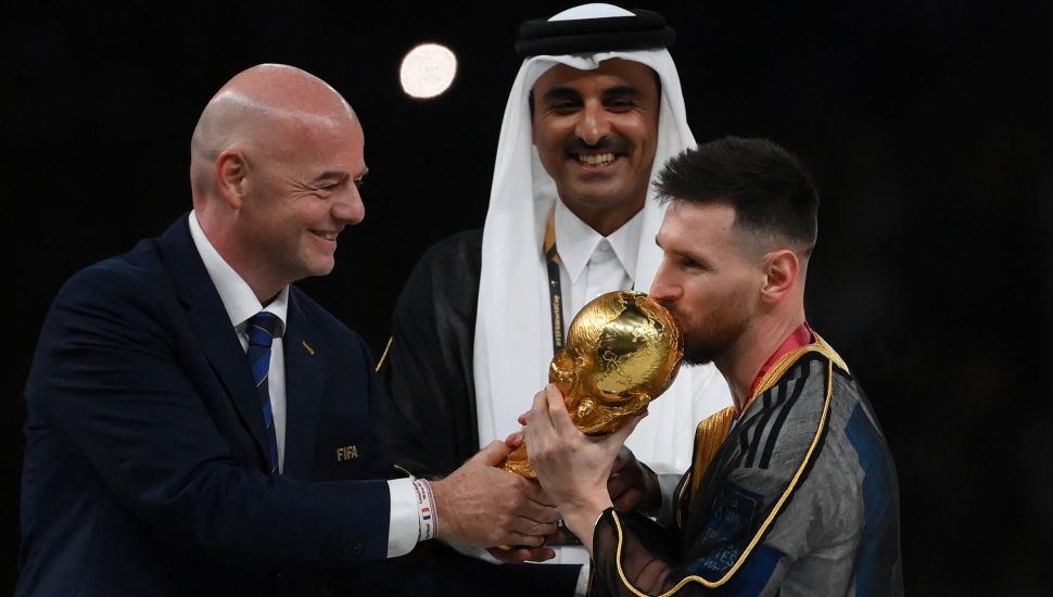 Pemain depan Argentina Lionel Messi mencium trofi Piala Dunia saat Presiden FIFA Gianni Infantino dan Emir Qatar Sheikh Tamim bin Hamad al-Thani terlihat pada upacara trofi Piala Dunia 2022 Qatar setelah pertandingan final antara Argentina dan Prancis di Stadion Lusail di Lusail, utara Doha, Qatar, Minggu (18/12/2022). [FRANCK FIFE / AFP]