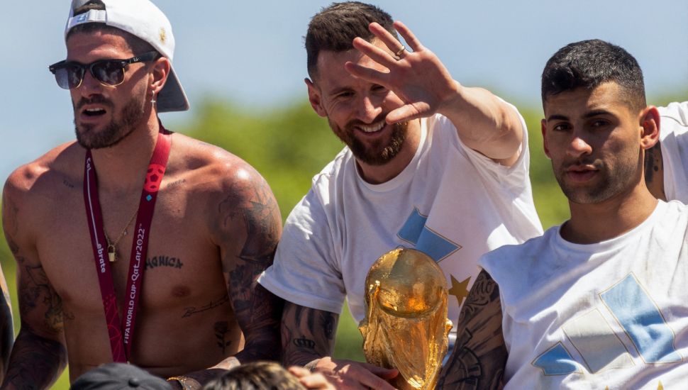 Pemain Argentina Rodrigo De Paul (Kiri), Lionel Messi (Tengah) dan Cristian Romero (Kanan) merayakan di atas bus dengan tanda bertuliskan "Juara Dunia" dengan pendukung setelah menjuarai turnamen Piala Dunia 2022 Qatar saat mereka melakukan tur keliling di pusat kota Buenos Aires, Argentina, Selasa (20/12/2022). [TOMAS CUESTA / AFP]