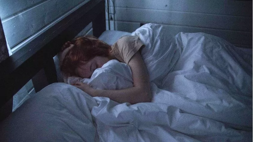 Wanita tidur nyenyak di kamar yang gelap dan tenang sebagai bagian rutinitas pemulihan tubuh harian yang optimal