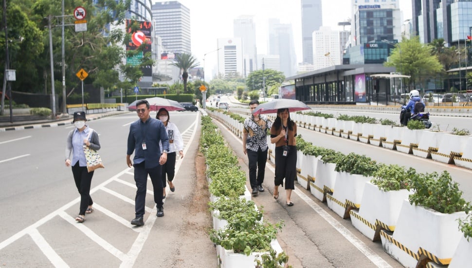 Pekerja melindungi tubuh dari terik matahari menggunakan payung saat berjalan di kawasan Sudirman, Jakarta, Kamis (21/12/2023). [Suara.com/Alfian Winanto]