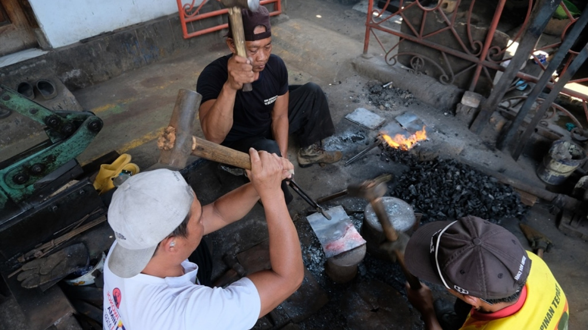 Tiga orang pekerja mnyelesaikan proses penempaan lempengan pelat besi untuk menjadi cangkul proyek [Diaz Abidin/Suara Semarang]