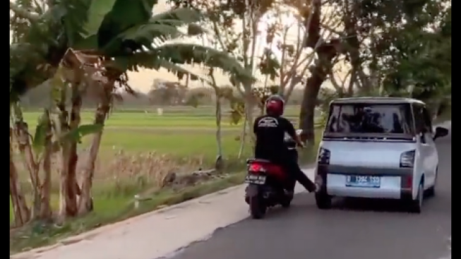 Ngakak, Pengendara Motor Dorong Mobil Listrik yang Mogok dengan Sebelah Kaki